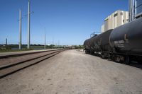 a train engine with its tank cars pulled along tracks in a rural setting near other railroad tracks