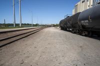 a train engine with its tank cars pulled along tracks in a rural setting near other railroad tracks