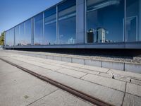 a train tracks that are next to a glass wall in a building with a city skyline in the background