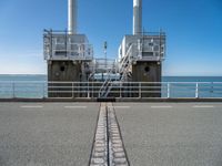 train tracks in front of a railing with the ocean behind them from a distance view