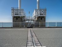 train tracks in front of a railing with the ocean behind them from a distance view