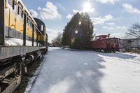 a train traveling down tracks with snow and trees behind it as the sun shines brightly on the left side