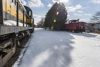 a train traveling down tracks with snow and trees behind it as the sun shines brightly on the left side