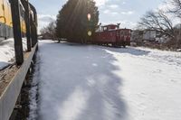 a train traveling down tracks with snow and trees behind it as the sun shines brightly on the left side