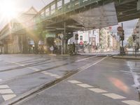 a train crossing under an overpass near a sidewalk and several people on bikes waiting