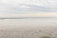 an empty sandy beach with a large body of water on the horizon, waves crashing in and out