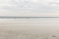 an empty sandy beach with a large body of water on the horizon, waves crashing in and out