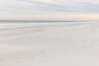 an empty sandy beach with a large body of water on the horizon, waves crashing in and out