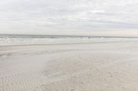 an empty sandy beach with a large body of water on the horizon, waves crashing in and out