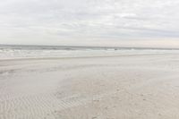 an empty sandy beach with a large body of water on the horizon, waves crashing in and out