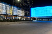 a street with a large light blue screen on the side of it next to a building