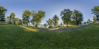 the sun reflects off the grassy ground as it casts shadows on trees and grass, with path leading up to large green hill