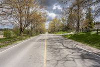 a street stretches to a country side with trees in the distance, while clouds cover the sky