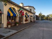 a sidewalk with flags outside a store on it's side and trees at its entrance