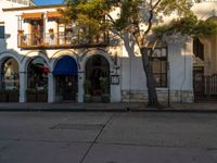 a man is sitting under a tree in front of a building that has an arched porch