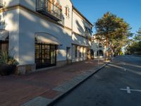 an empty sidewalk in the shadow by a building that has several shops and apartments on it