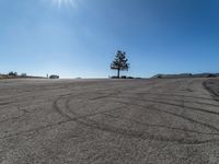 a car parked in a large empty lot near a tree and cars driving by it