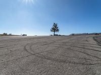 a car parked in a large empty lot near a tree and cars driving by it