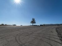 a car parked in a large empty lot near a tree and cars driving by it