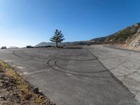 a road with two lines drawn in a circle near a tree and a hill with hills in the background