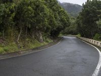 a mountain road with steep hillside and trees next to it and a hill top on the right