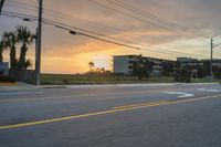 the sun sets behind apartment buildings near an empty road in florida during a tropical sunset