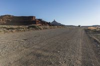 a truck drives down a dusty road with a mountain in the back ground behind it