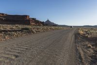 a truck drives down a dusty road with a mountain in the back ground behind it