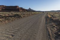 a truck drives down a dusty road with a mountain in the back ground behind it