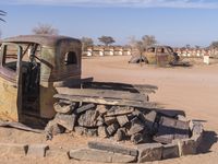 an old truck is parked in the desert near some plants and rocks, with a broken tire