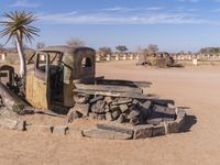 an old truck is parked in the desert near some plants and rocks, with a broken tire