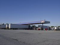 trucks and trailers sit in a parking lot as a person stands next to the truck in front of the gas station