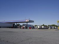 trucks and trailers sit in a parking lot as a person stands next to the truck in front of the gas station