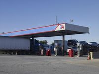 trucks and trailers sit in a parking lot as a person stands next to the truck in front of the gas station