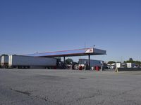 trucks and trailers sit in a parking lot as a person stands next to the truck in front of the gas station