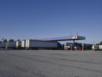 trucks and trailers sit in a parking lot as a person stands next to the truck in front of the gas station