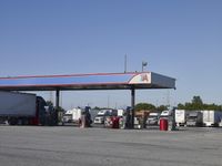 trucks and trailers sit in a parking lot as a person stands next to the truck in front of the gas station