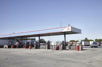 trucks and trailers sit in a parking lot as a person stands next to the truck in front of the gas station