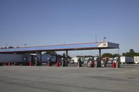 trucks and trailers sit in a parking lot as a person stands next to the truck in front of the gas station