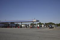 trucks and trailers sit in a parking lot as a person stands next to the truck in front of the gas station