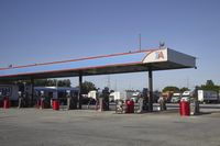 trucks and trailers sit in a parking lot as a person stands next to the truck in front of the gas station