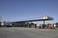 trucks and trailers sit in a parking lot as a person stands next to the truck in front of the gas station