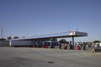 trucks and trailers sit in a parking lot as a person stands next to the truck in front of the gas station