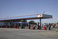 trucks and trailers sit in a parking lot as a person stands next to the truck in front of the gas station