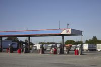 trucks and trailers sit in a parking lot as a person stands next to the truck in front of the gas station