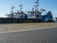 three tug boats docked by a building next to a road with a light on top