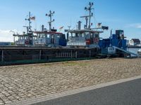 three tug boats docked by a building next to a road with a light on top