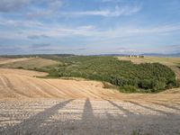 the shadow of a person standing on a road looking over a rural area with hills