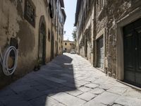 an alley with a bicycle that's attached to a building, along which is a street with a hose