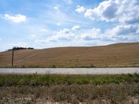 this image is looking at the empty rural road beside the field with fields in the distance